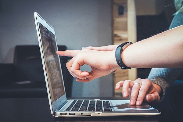 Laptop seitlich, eine Person deutet auf den Bildschirm